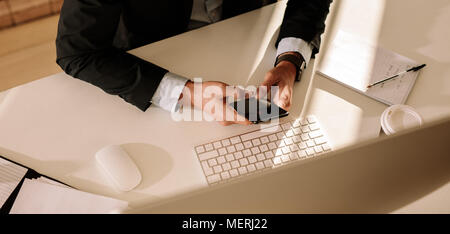 Vista dall'alto di imprenditore lavora su telefono cellulare seduti al tavolo di lavoro. Uomo di funzionamento telefono mobile seduti nella parte anteriore del computer. Foto Stock