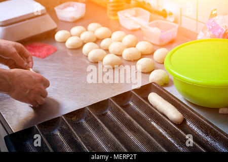 Un close-up di una femmina di bakerpulls l'impasto per la cottura di focacce di hotdog su un metallo becary tabella con un mattarello Foto Stock