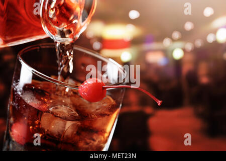 Il whiskey è versata da una caraffa in un bicchiere con ghiaccio.Cocktail Manhattan con cherry. Foto Stock