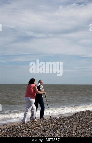 Coppia di anziani camminando lungo la riva del mare sulla spiaggia di ciottoli a sizewell suffolk in Inghilterra Foto Stock