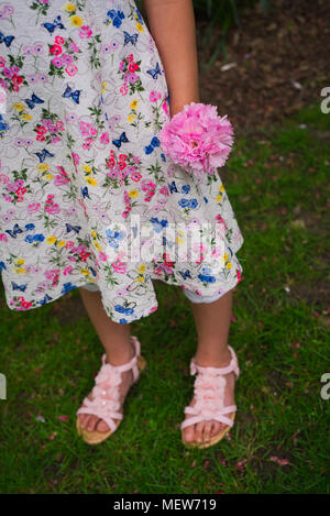 Ragazza in abito floreale tenendo un piccolo bouquet di fiori di colore rosa Foto Stock