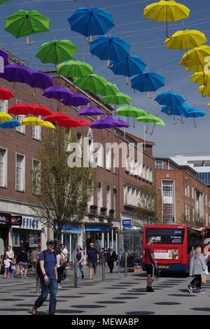 Venditore di palloncino in Exeter High Street, con la Exeter Riddle Obelisco Scultura e coloratissima primavera ombrelloni. Devon, Regno Unito. Aprile, 2018. Foto Stock