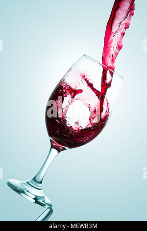 Onda formata sul versamento di vino rosso su un bicchiere da degustazione contro uno sfondo blu Foto Stock