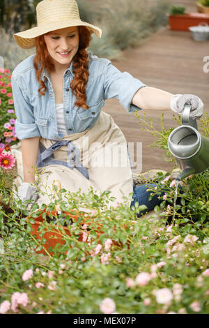 Giardiniere sorridente donna fiori di irrigazione in giardino Foto Stock