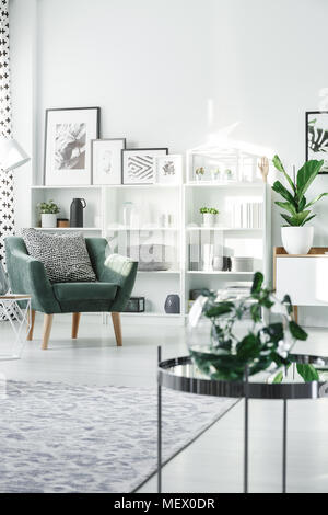 Poltrona verde di bianco e nero con cuscino in piedi in salotto luminoso interno con poster e rack con decor Foto Stock