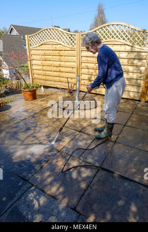 Donna anziana di lavaggio a spruzzo di un patio con la rondella di pressione all'inizio dell'estate Inghilterra REGNO UNITO Foto Stock