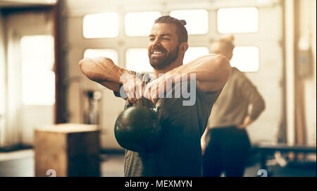 Montare il giovane uomo in sportswear sorridente e sollevamento manubri durante un esercizio di classe in una palestra Foto Stock