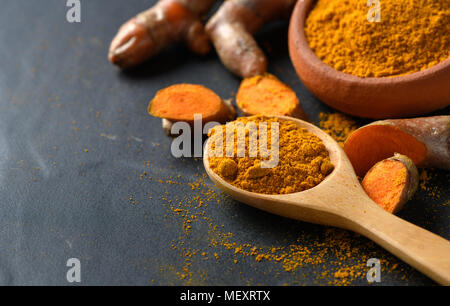 La curcuma in polvere in cucchiaio di legno sulla tavola nera, le spezie e le erbe concept Foto Stock