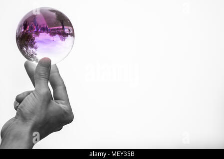 Uomo con mani rosso vestito come il diavolo trattiene e gioca con un vetro isolato sfera di cristallo contenente le riflessioni di persone Foto Stock