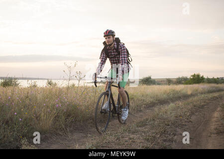 Giovane uomo traveler ride all'aperto sulla bicicletta da ciclocross rider in abbigliamento casual con zaini Foto Stock