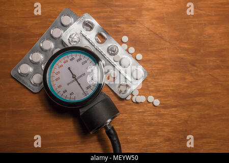 Sfigmomanometro con due alveoli di medicina bianco droga e compresse sparsi sul vecchio tavolo in legno. La scena prima della misurazione di arteriosa blo Foto Stock