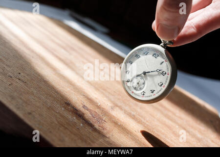 Tenere le dita vintage orologio da tasca con vetro rotto sopra il vecchio Dirty superficie in legno Foto Stock