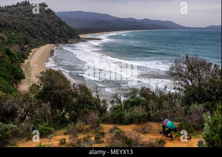 Un uomo corse in mountain bike su un sentiero costiero che si affaccia sul Mar Mediterraneo nei pressi di Punta Ala in Toscana. L'Italia. Foto Stock