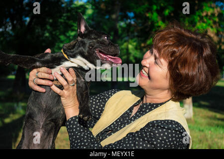 Ritratto di sorridere, allegro donna attesa, kissing pet, Cane in camera. Nero, attivo, curiosi bulldog francese. Caucasici, anziani mamma casalinga che guarda a Foto Stock