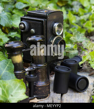 Retrò macchina fotografica e binocolo e pellicole fotografiche in un giardino di edera. Foto Stock