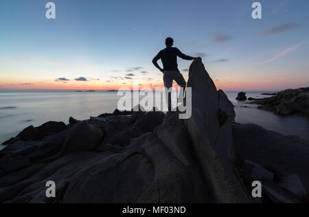 Un turista su scogliere ammira i colori del tramonto sul mare blu Punta Molentis Villasimius Cagliari Sardegna Italia Europa Foto Stock