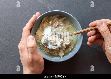 Zuppa asiatica di anatra con mani di uomo nero su sfondo di pietra Foto Stock