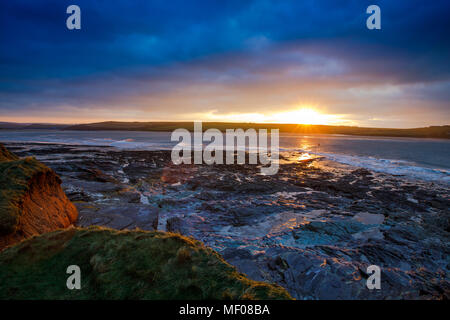 Il sole che tramonta sulla Baia di Daymer in Cornovaglia (UK) con la bassa marea. Foto Stock