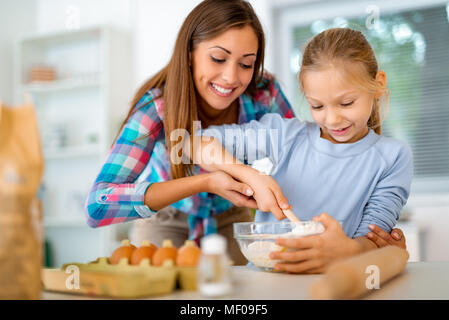 La madre e la bambina di miscelazione di pasta nella cucina domestica. Madre impara a sua figlia come fare i biscotti. Foto Stock