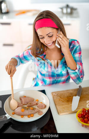 Giovane e bella donna che fa il pasto sano nella cucina domestica. Ella si utilizza lo smartphone per controllare una ricetta per il pasto si prepara. Foto Stock