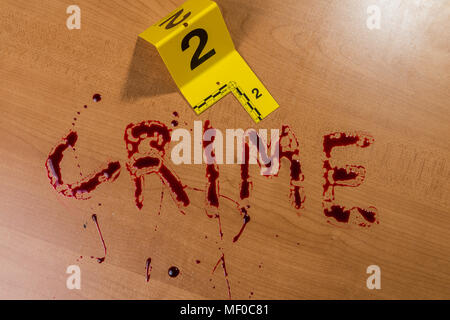 La parola “crimine” è scritta nel sangue su una superficie di legno accanto a un coltello sanguinoso, entrambi contrassegnati da marcatori di evidenza della scena del crimine. Foto Stock
