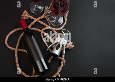 Rosso bottiglia di vino, due bicchieri e cavatappi su sfondo nero. Vista da sopra con lo spazio di copia Foto Stock