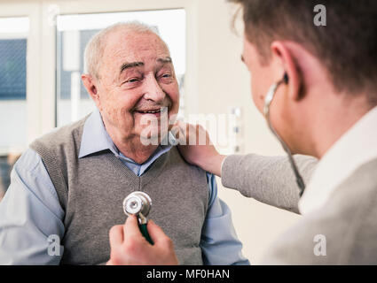 Senior uomo sorridente in un infermiere con uno stetoscopio a casa Foto Stock