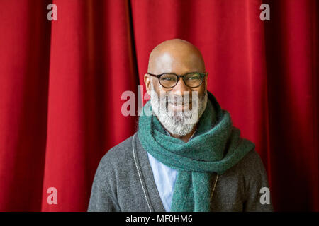 Ritratto di uomo sorridente con gli occhiali e sciarpa in parte anteriore del sipario rosso Foto Stock