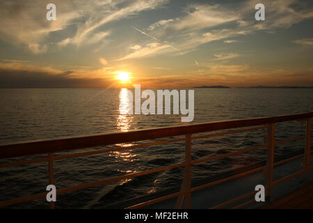 Dal ponte di una nave da crociera al tramonto guardando oltre oceano verso terra in distanza. Foto Stock