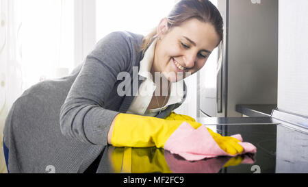 Bella donna sorridente pulizia sporco macchiato piano cottura elettrico su cucina Foto Stock