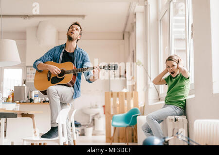 Inorridito figlio che copre le sue orecchie con il padre a suonare la chitarra a casa Foto Stock