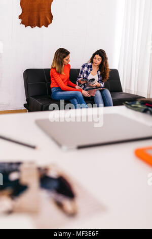 Due stilisti di moda di seduta sul lettino in studio a discutere di tessuto Foto Stock