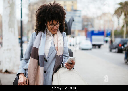 Spagna, Barcellona, Donna sorridente con un telefono cellulare e gli auricolari in città Foto Stock