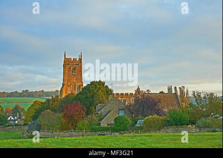 Sud rurale scena Warwickshire withSt Pietro chiesa nel villaggio di Long Compton con la mattina presto il sole illumina il campanile di una chiesa Foto Stock