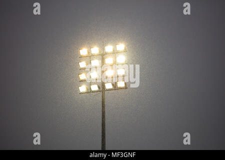 Le luci dello stadio in pole, all'aperto, innevate di notte. Cielo scuro in contrasto a luci intense. Foto Stock