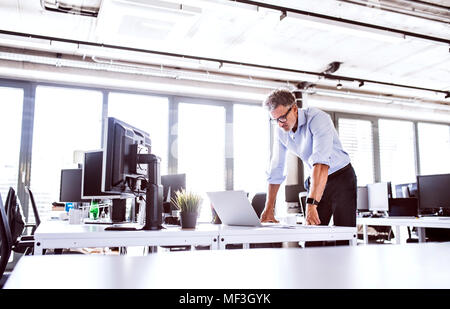 Imprenditore maturo guardando il laptop sulla scrivania in ufficio Foto Stock