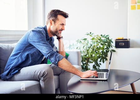 Uomo sorridente seduto sul divano con laptop Foto Stock