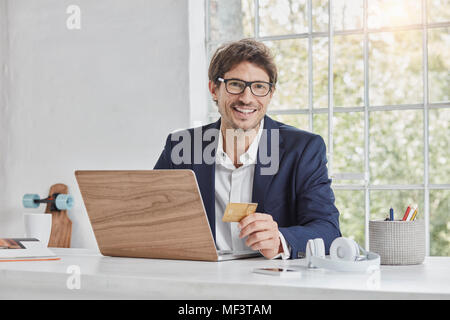Ritratto di imprenditore sorridente con notebook sulla scrivania con carta di credito Foto Stock
