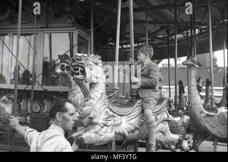 1948, il giovane ragazzo che indossa uniformi scolastiche a cavallo di un drago di legno su una fiera del divertimento merry-go-round, Londra, Inghilterra, Regno Unito. Foto Stock