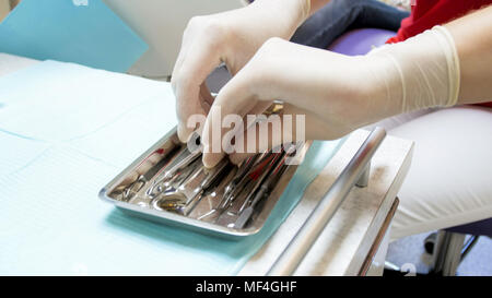 Primo piano immagine di dentista in mano dei guanti di protezione in lattice tenendo strumenti sterili dal vassoio Foto Stock