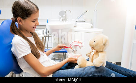 Carina ragazza sorridente seduto in poltrona del dentista e giocare con Teddy bear Foto Stock