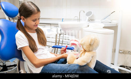 Ritratto di Cute girl gioca con Teddy bear in studio dentistico e mostrando come pulire i denti Foto Stock