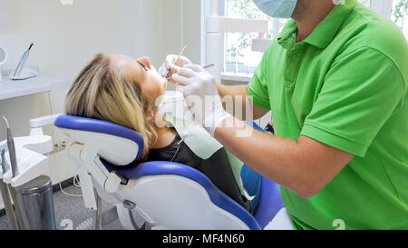 Ritratto di giovane donna bionda giacente in poltrona del dentista mentre medico ispeziona i suoi denti Foto Stock