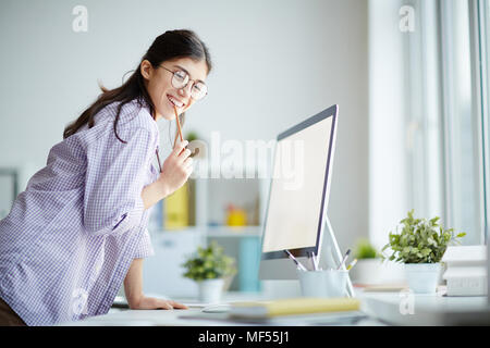 Ritratto di successo della giovane designer in piedi nella parte anteriore del computer e sorridente Foto Stock