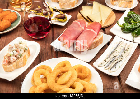 La cucina di Spagna. Una foto di molti diversi tapas spagnole al buio su un rustico texture. Jamon, formaggio, vino, crocchette, anelli di calamari, acciughe e mo Foto Stock