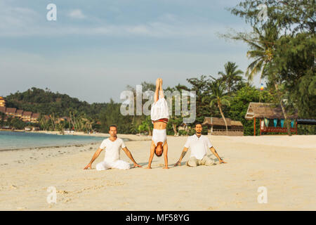 Thailandia Koh Phangan, tre persone fare yoga su una spiaggia Foto Stock