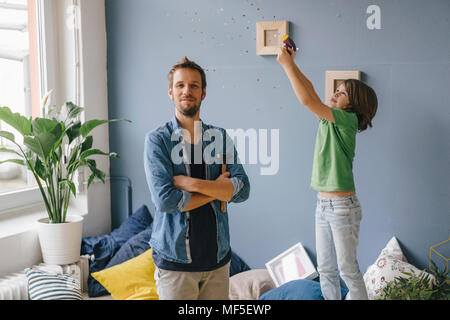 Figlio soffiando coriandoli sopra orgoglioso padre tenendo un martello a casa Foto Stock