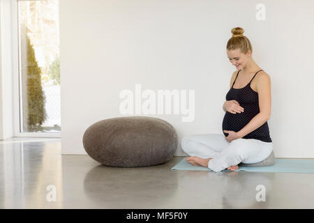 Sorridente incinta Donna seduta su un materassino yoga Foto Stock