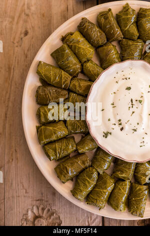 Vista superiore colpo di ripieni di foglie di uva dolma sul piatto rotondo con yogurt al centro della piastra. Foto Stock