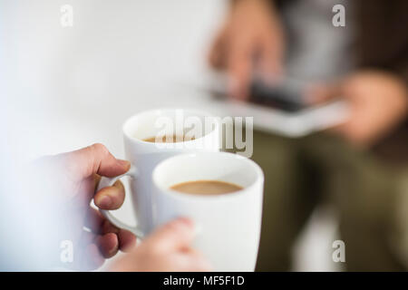 Close-up di donna azienda tazze da caffè mentre l'uomo utilizzando tablet in ufficio Foto Stock